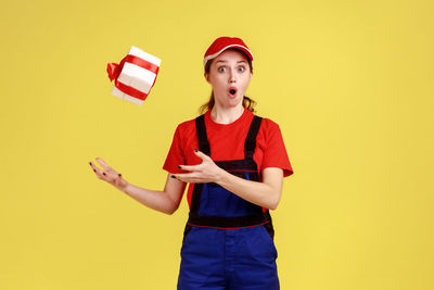 Portrait of young woman holding box while standing against yellow background