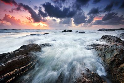 Long exposure of waves splashing over rocks in sea during sunset