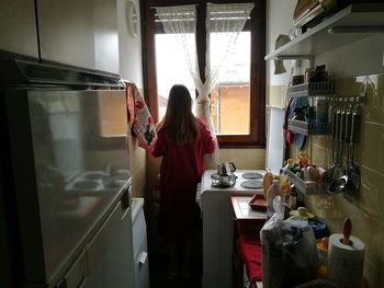 Rear view of girl looking through window in kitchen