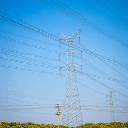 Low angle view of electricity pylon against clear blue sky