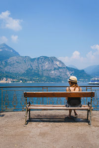 Man sitting on bench looking at mountains against sky