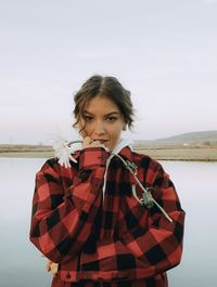 Portrait of young woman standing by river against sky