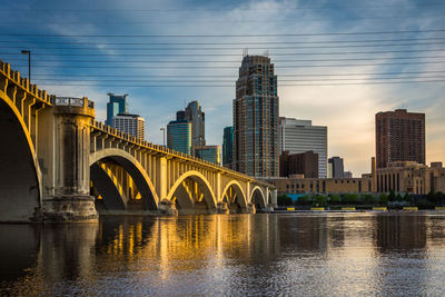 Bridge over river by buildings against sky in city