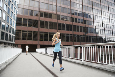 Mature blond woman jogging against businesswoman on footbridge in financial district