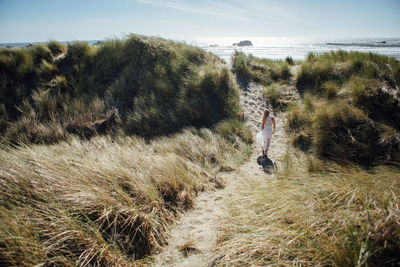 Rear view of young woman walking on trail leading towards beach