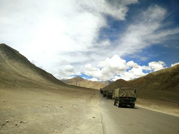 Military trucks on mountain road against sky