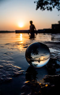 Reflection of silhouette person on beach against sky during sunset