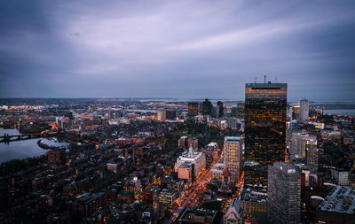 Aerial view of illuminated city buildings against cloudy sky at dusk