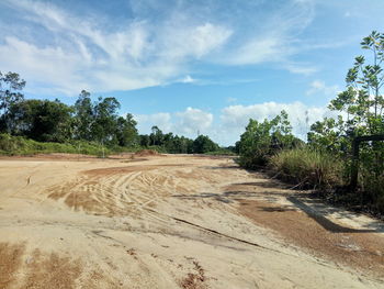 Dirt road amidst trees on field against sky