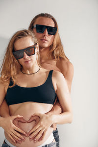 Portrait of young woman wearing sunglasses against white wall