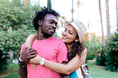 Side view of loving multiracial couple of travelers standing in park with palms and holding hands while looking at each other