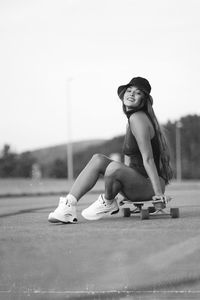 Portrait of young woman sitting on skateboard outdoors