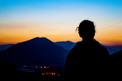 Silhouette of a woman looking at mountains against sky during sunset