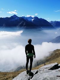 Rear view of man standing on rock looking at mountains