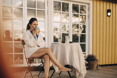 Full length of mature woman drinking coffee while sitting at patio in holiday villa