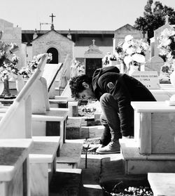 Sad young man sitting amidst tombstones in cemetery