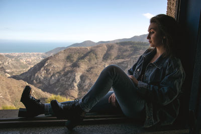 Side view of woman sitting on mountain against sky