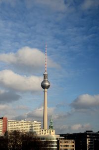 Communications tower in city against cloudy sky