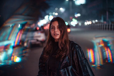Portrait of woman standing against illuminated building at night