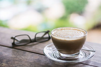 Close-up of cappuccino by eyeglasses on table