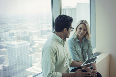 Business people with digital tablet sitting on window sill, discussing