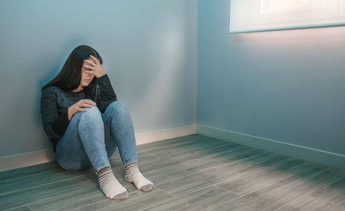 Depressed woman sitting against wall