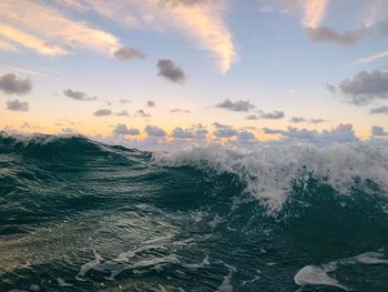Wave splashing water in sea against sky during sunset