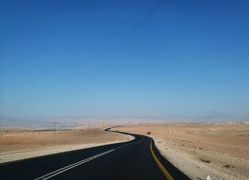 Road amidst desert against clear blue sky