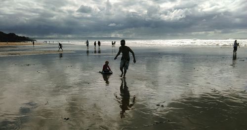 People at beach against cloudy sky