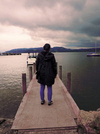 Rear view of man standing on pier over lake against sky