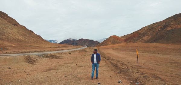 Man standing on dirt road amidst mountains against sky