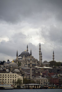 Mosque in city against cloudy sky