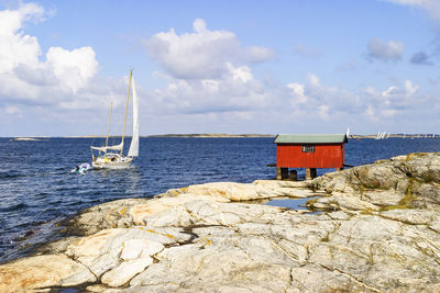 Red boathouse on a rock by the sea and a sailboat