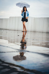 Full length of young woman standing on building terrace during rainy season