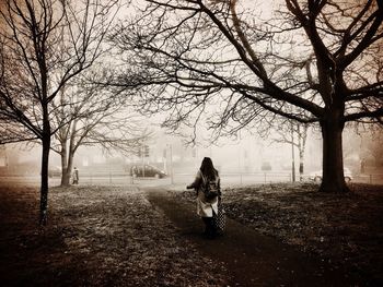 Rear view of woman walking on bare tree in park