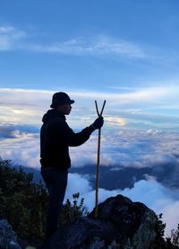 Side view of young man standing by cliff against sky