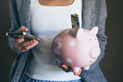 Closeup woman holding happy piggy bank and using mobile phone. female saving money