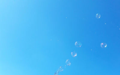 Low angle view of bubbles against clear blue sky