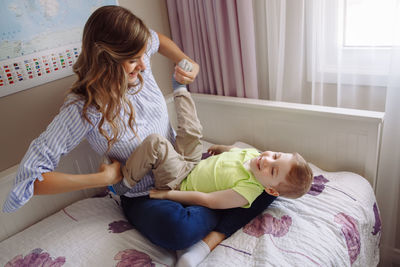 Mother playing with son on bed at home