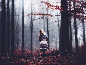 Rear view of man standing by tree in forest