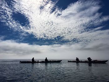 Silhouette people in sea against sky