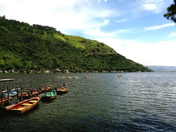 Boats moored in calm lake against mountain range