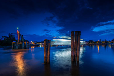 Illuminated wooden posts in lake against sky at night