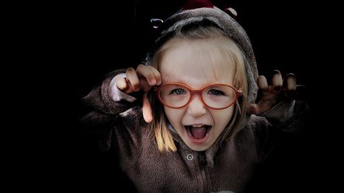 Portrait of girl wearing hooded shirt gesturing against black background