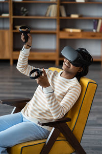 Happy young african american woman wearing virtual reality goggles playing video games at home