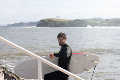 Wet young man coming out of the water after surfing watch the time