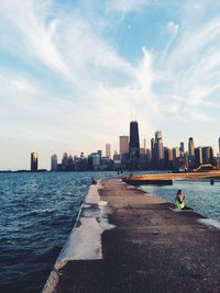 People sitting on jetty at sea against buildings