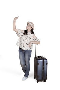 Woman taking selfie with suitcase against white background