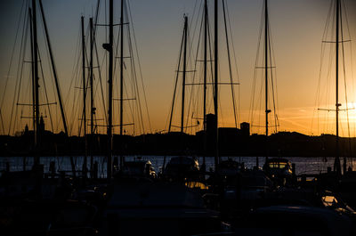 Silhouette sailboats in harbor against sky at sunset