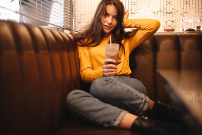 Teenage girl holding chocolate milkshake while sitting in cafe